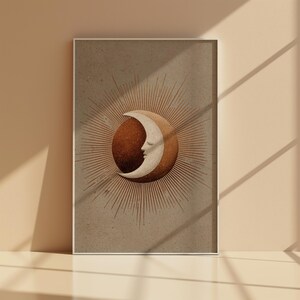 Könnte beinhalten: Ein gerahmter Kunstdruck mit einem Himmelsmotiv. Das Kunstwerk zeigt einen Halbmond mit Gesicht, vor einer braunen Kugel, umgeben von Strahlenlinien. Die Farbpalette umfasst Braun-, Beige- und Weißtöne und erzeugt eine Vintage-Ästhetik.
