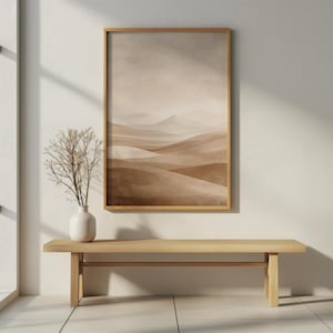 Könnte beinhalten: Ein gerahmter Kunstdruck mit einer Landschaft in Braun- und Beigetönen, die sanfte Hügel und Berge zeigt. Er hängt über einer hellen Holzbank. Eine weiße Vase mit getrockneten Zweigen steht auf der Bank.