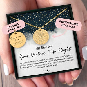 May include: A gold necklace with a star map pendant and a smaller pendant with the text "Forever proud of you 04.12.2023". The necklace is in a black box with a white background and the text "On this day your venture took flight" and "Personalized star map".