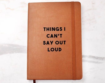 May include: A brown leather-bound journal with the text "THINGS I CAN'T SAY OUT LOUD" printed in black on the front cover.