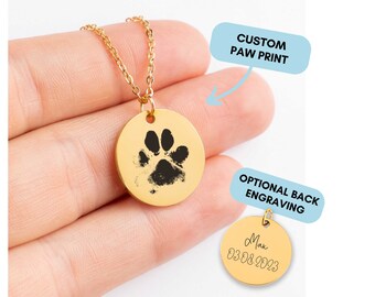 May include: Gold necklace with a round pendant featuring a black paw print. The back of the pendant can be engraved with a name and date.  "CUSTOM PAW PRINT" and "OPTIONAL BACK ENGRAVING" are written in blue text on the image.