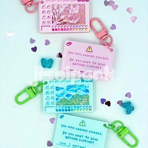 Könnte beinhalten: Eine Sammlung von Schlüsselanhängern mit rosa und grünen Karabinerhaken. Die Schlüsselanhänger zeigen computerbezogene Designs, darunter ein Fenster mit einer Landschaft und eine Popup-Nachricht mit der Aufschrift "You have unsaved changes. Do you want to save before closing?"