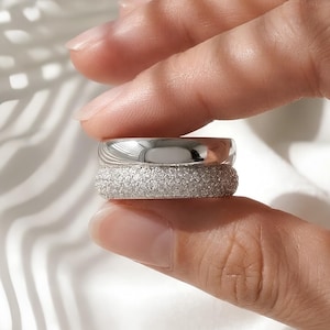 May include: A set of two stacked rings featuring a smooth, polished silver-toned band on top and a wider, textured band with a granular, sparkling surface finish on the bottom. The rings are held together, showcasing their contrasting metallic textures.