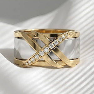 May include: A wide band ring featuring a polished silver-tone center band layered with two intersecting gold-tone bands. One of the gold-tone bands is embellished with a row of small, clear, round-cut stones set along its entire length.