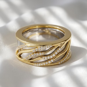 May include: A wide band ring featuring a two-tone design with a polished silver-colored inner band and a gold-colored outer layer. The gold-colored exterior is crafted with open, wavy, flowing lines that are encrusted with small, clear, round stones.