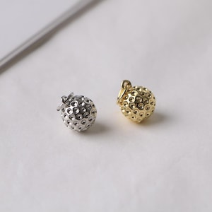 May include: Two small, round, golf ball-shaped charms. One is silver-colored, and the other is gold-colored. Each charm has a small loop at the top for attaching to a chain or bracelet. The charms are on a white surface.