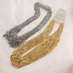 Puede incluir: Vista aérea de tres conjuntos de collares. Uno es plateado, dos son dorados. Los collares son cadenas finas. Hay una etiqueta que dice "Fashion Jewelry".