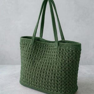 May include: A green crochet tote bag with two long handles. The bag has a textured, open weave pattern and a rectangular shape. The bag is made of a soft, durable material, perfect for carrying everyday items.