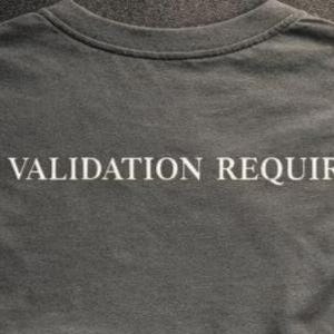 May include: A dark gray t-shirt with the phrase "NO VALIDATION REQUIRED" printed in white capital letters across the back. The shirt has a crew neck and short sleeves, and the fabric appears to be soft.