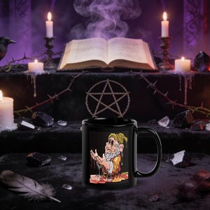 Pode incluir: Caneca de cerâmica preta com um desenho de um anão com chapéu verde e roupa laranja. A caneca está sobre uma mesa preta com velas acesas, um livro aberto e um pentagrama. Dois corvos pretos estão empoleirados.