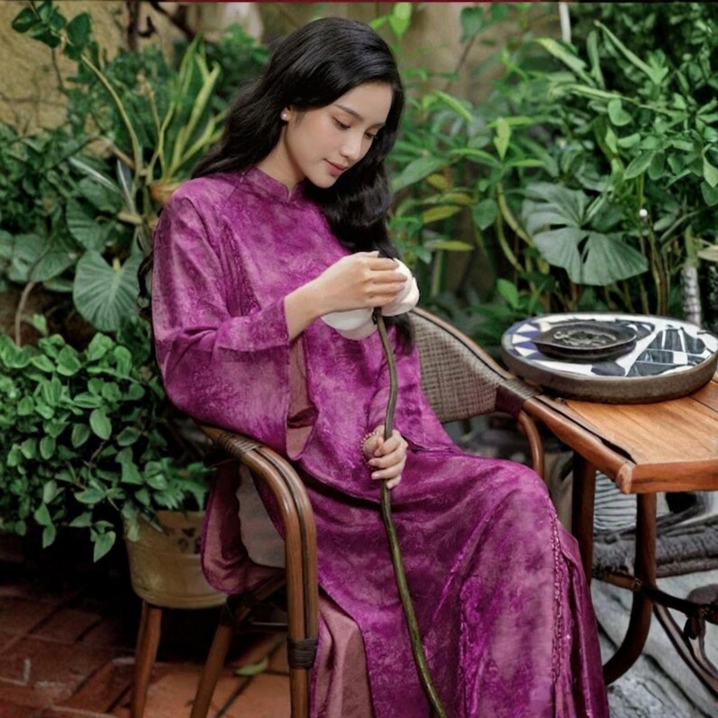 Peut inclure: Une robe longue violette &agrave; manches longues avec un col montant et une texture subtilement marbr&eacute;e. Le v&ecirc;tement pr&eacute;sente une silhouette ample et fluide avec des manches longues et un ourlet droit, confectionn&eacute; dans un tissu l&eacute;ger et brillant.