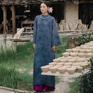 Peut inclure: Une tunique bleue longue jusqu'aux pieds, &agrave; manches longues, dot&eacute;e d'un motif textur&eacute; subtil, d'un col montant et d'une encolure simple. Le v&ecirc;tement est associ&eacute; &agrave; un pantalon magenta uni et ample qui tombe jusqu'au sol, cr&eacute;ant une silhouette superpos&eacute;e.