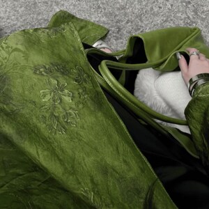 Peut inclure: Un grand sac fourre-tout vert olive pr&eacute;sentant une surface textur&eacute;e avec un motif floral ton sur ton subtil. Le sac est dot&eacute; de deux bandouli&egrave;res et d'un compartiment int&eacute;rieur spacieux contenant une doublure blanche douce et un insert noir.