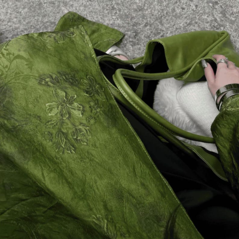 Peut inclure: Un grand sac fourre-tout vert olive pr&eacute;sentant une surface textur&eacute;e avec un motif floral ton sur ton subtil. Le sac est dot&eacute; de deux bandouli&egrave;res et d'un compartiment int&eacute;rieur spacieux contenant une doublure blanche douce et un insert noir.