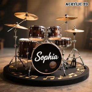 May include: A complete drum set with brown wooden drums, cymbals, and stands. The bass drum features the name "Sophia" in white script. The set is on a black mat with gold musical notes. The text "ACRYLIC 2D" is in the top right corner.
