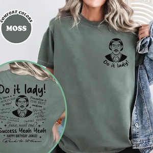 Puede incluir: Camiseta verde musgo con el texto "Do it lady!" y un gráfico de un hombre con gafas y bigote. La parte posterior de la camisa tiene texto y gráficos adicionales. La camisa es de color confort.