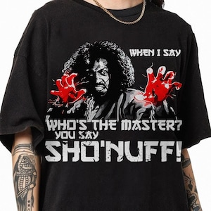 May include: Black t-shirt featuring a graphic of a man with red hands and the text "WHEN I SAY WHO'S THE MASTER? YOU SAY SHO'NUFF!". The design is in black and white with red accents. The shirt has short sleeves and a round neckline.