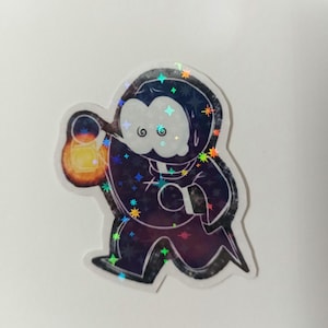May include: Holographic sticker of a cartoon figure in a dark cloak, carrying a glowing lantern. The figure has a white face with swirling eyes. The sticker has a starry, galaxy-like design with colourful accents.