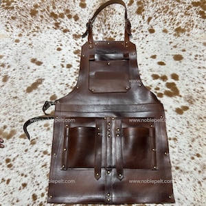 May include: A brown leather apron with multiple pockets and adjustable straps. The apron has a large chest pocket and two lower pockets, all secured with rivets. The apron is designed for durability and functionality, suitable for various crafts or culinary uses.