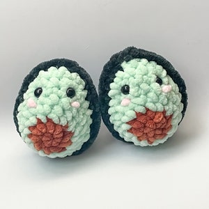May include: Two crocheted avocado plush toys with black yarn for the pit and green yarn for the avocado flesh. Each avocado has a cute face with black eyes and pink cheeks.