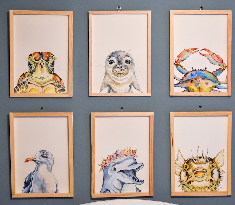 May include: A set of 8 framed watercolor paintings featuring various sea creatures. The paintings include a sea turtle, a seal, a crab, a seagull, a dolphin, and a fish.