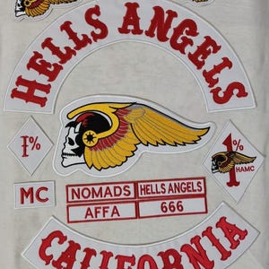 May include: White fabric with embroidered patches featuring the words "HELLS ANGELS" in red, arched across the top and "CALIFORNIA" at the bottom. A skull with wings is a central design element, along with the text "NOMADS", "AFFA", and "666".