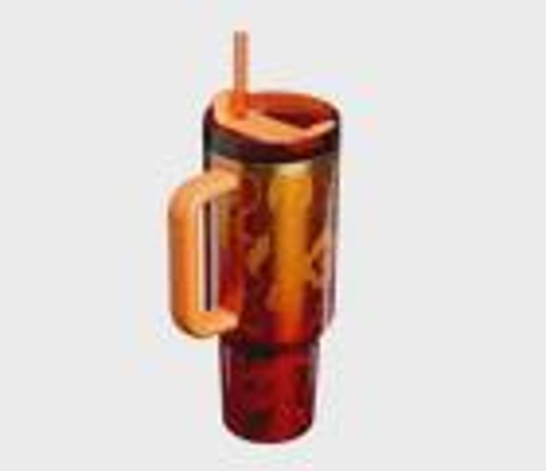May include: A translucent amber-colored tumbler with a dark red base and a lighter orange handle. The drinkware features a matching orange lid with an integrated straw and a vertical orange graphic design on the side of the main cylindrical body.