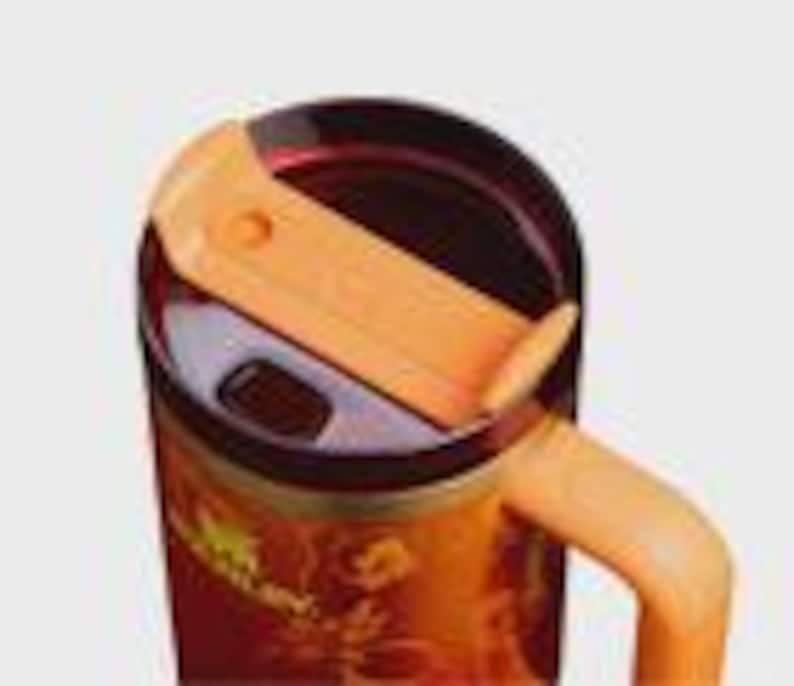 May include: A stainless steel tumbler featuring a dark orange and red floral pattern with the Stanley logo printed on the side. The tumbler includes a dark translucent lid with a light orange sliding closure and a matching light orange handle.