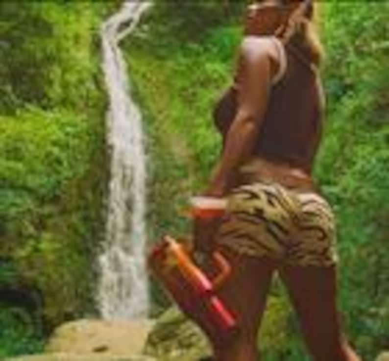 May include: A pair of shorts featuring a black and tan tiger stripe pattern, paired with a dark brown sleeveless top. The shorts have a fitted silhouette and are worn with a bright orange and red plastic water gun held in the hand.
