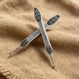 May include: Two silver-toned metal seam rippers with ornate floral engravings at the ends. One tool features the engraved text My happy place is sewing. Both tools have a pointed metal tip with a small red safety ball at the base of the blade.