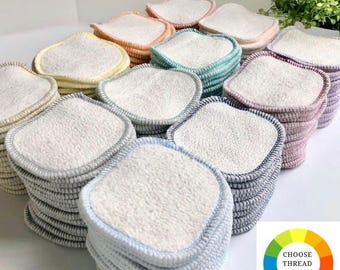 May include: A collection of square, white, textured fabric pads stacked in multiple piles. Each pile features a distinct colored stitched border, including yellow, orange, teal, purple, and blue. A color wheel graphic with the text CHOOSE THREAD COLOR.