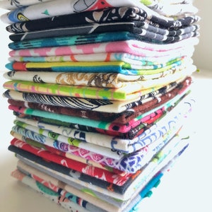 May include: A tall, vertical stack of folded fabric squares featuring a diverse array of colourful patterns, including geometric shapes, floral motifs, and abstract designs in shades of blue, red, green, yellow, pink, black, and white.