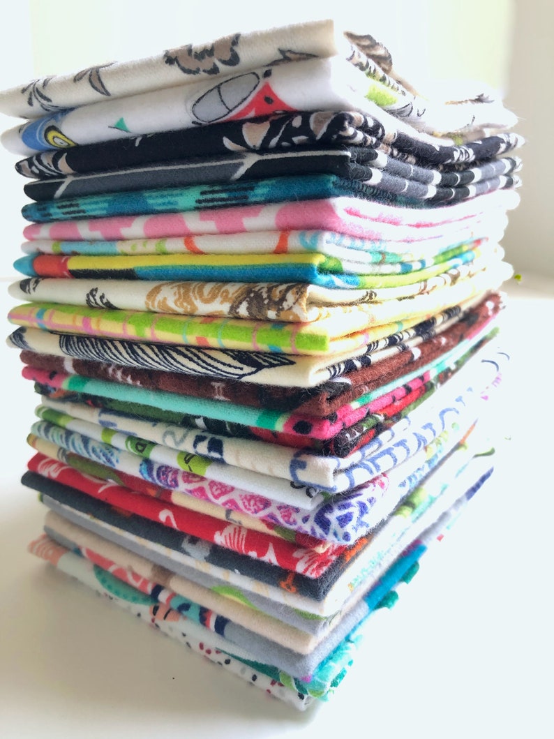 May include: A tall, vertical stack of folded fabric squares featuring a diverse array of colourful patterns, including geometric shapes, floral motifs, and abstract designs in shades of blue, red, green, yellow, pink, black, and white.
