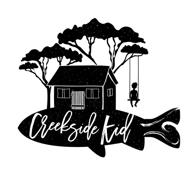 A black and white illustration depicting a house, trees, and a person on a swing, with the text "Creekside Kid" written on the fish-shaped object.