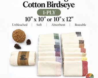 May include: Unbleached organic cotton birdseye 1-ply cloths in 10 x 10 inches or 10 x 12 inches. The set includes folded cream-colored cloths with various colored stitched edges, a rolled cloth with a paper band, and decorative pinecones.