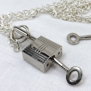 May include: A silver padlock with a key attached to it, hanging from a silver chain. The padlock and chain are on a white surface.