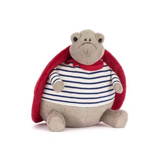 Könnte beinhalten: Ein Plüschtier in Form einer Schildkröte mit grauem Kopf und Körper, bekleidet mit einem gestreiften blau-weißem Hemd, einem roten Schal und einem roten Umhang. Das Spielzeug ist weich und kuschelig.