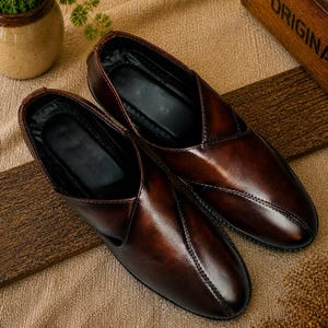 Puede incluir: Un par de zapatos sin cordones de cuero marr&oacute;n con un acabado brillante. Los zapatos tienen un dise&ntilde;o cl&aacute;sico con un detalle de costura y un interior oscuro. Se exhiben sobre una superficie texturizada.
