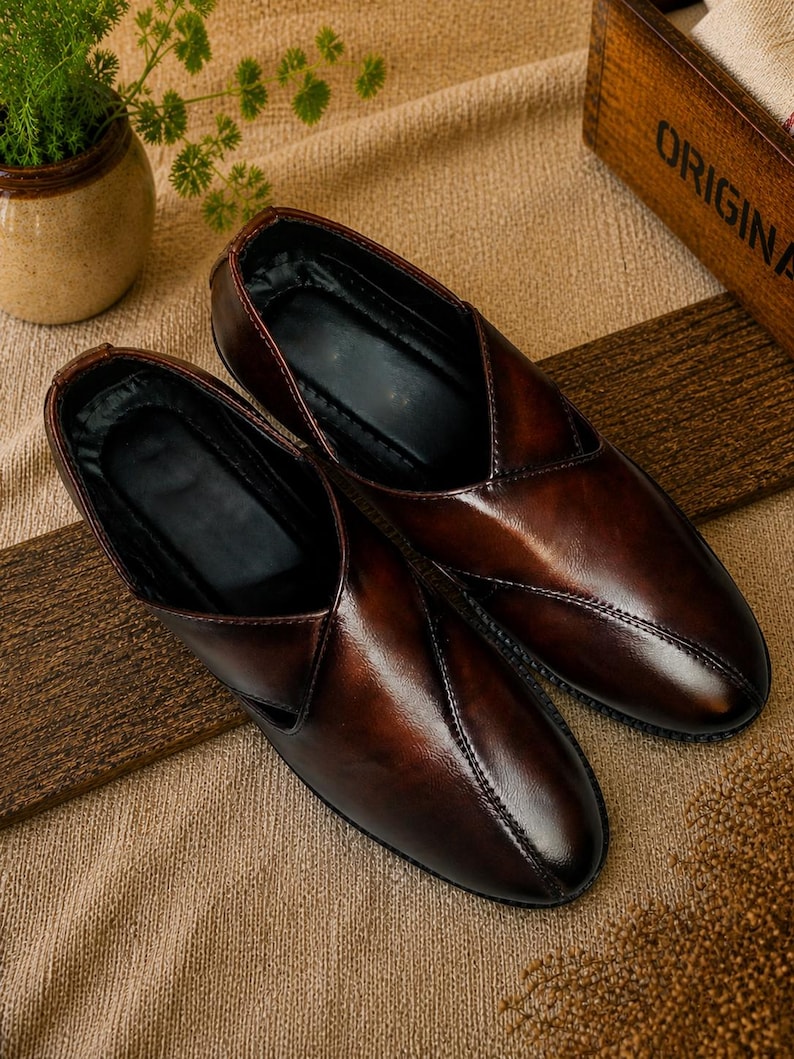 Puede incluir: Un par de zapatos sin cordones de cuero marr&oacute;n con un acabado brillante. Los zapatos tienen un dise&ntilde;o cl&aacute;sico con un detalle de costura y un interior oscuro. Se exhiben sobre una superficie texturizada.
