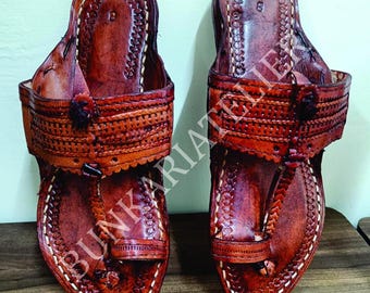 May include: A pair of brown leather sandals featuring intricate hand-tooled patterns, a toe loop, and a wide strap across the instep. The footbed is embossed with the number 8, and the text BUNKARIATELIER is visible across the center of the image.