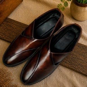 Puede incluir: Un par de zapatos sin cordones de cuero marr&oacute;n con un acabado brillante. Los zapatos tienen un dise&ntilde;o de punta puntiaguda y est&aacute;n colocados sobre una superficie texturizada. Los zapatos son de color marr&oacute;n oscuro.