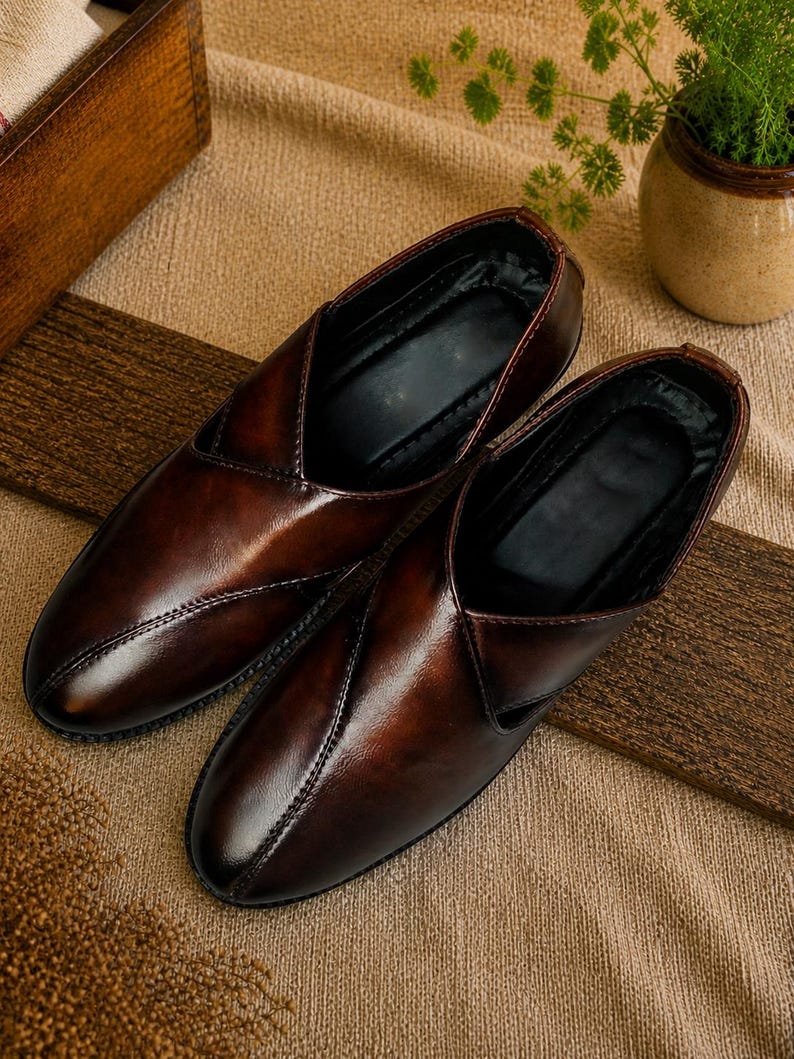 Puede incluir: Un par de zapatos sin cordones de cuero marr&oacute;n con un acabado brillante. Los zapatos tienen un dise&ntilde;o de punta puntiaguda y est&aacute;n colocados sobre una superficie texturizada. Los zapatos son de color marr&oacute;n oscuro.
