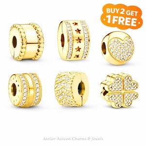 Op de afbeelding: Een verzameling goudkleurige bedel kralen met verschillende ontwerpen. Sommige kralen hebben heldere kristallen accenten, terwijl andere ster-, hart- en klaverpatronen hebben. De tekst "BUY 2 GET 1 FREE" is inbegrepen.