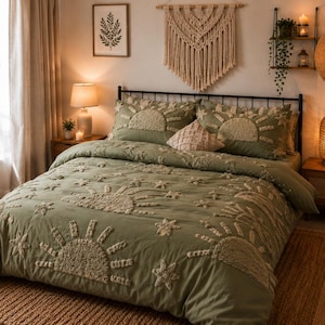 May include: A sage green duvet cover and pillowcases featuring embroidered sun and star patterns. The bedding is on a black metal bed frame. A woven rug is on the floor. The room is decorated with a macrame wall hanging and a woven pendant light.