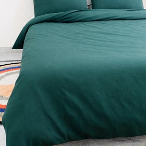 May include: A dark teal bed set, including a duvet cover and two pillowcases, on a black metal bed frame. The bedding is a solid color, with a smooth, slightly textured appearance. The bed is set on a colorful rug.