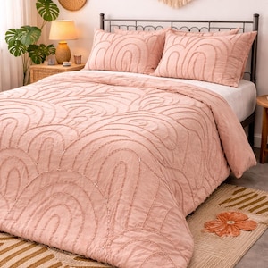 Puede incluir: Un edredón rosa rubor y dos fundas de almohada a juego con un diseño de arco bordado. La cama está hecha con una sábana blanca y se encuentra sobre una alfombra tejida con un patrón geométrico. Un dormitorio de estilo boho con una paleta de colores neutros.