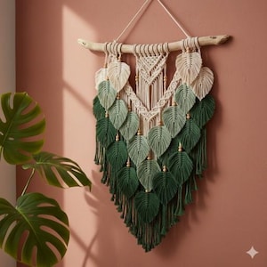May include: Macrame wall hanging featuring a leaf design in shades of green and cream. The leaves are arranged in a cascading pattern, with a wooden dowel at the top for hanging. The piece adds a touch of bohemian style to any room.