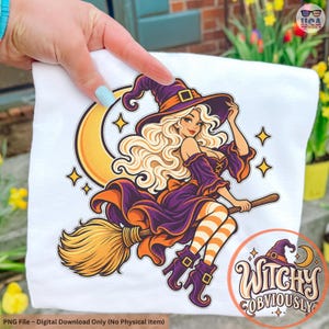 May include: A white t-shirt featuring a graphic illustration of a blonde witch wearing a purple hat and dress, riding a broomstick in front of a yellow crescent moon. The design includes orange and white striped stockings and the text Witchy Obviously.