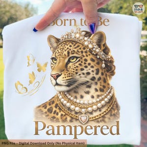 May include: White t-shirt featuring a regal leopard illustration. The leopard is adorned with a jeweled crown and pearl necklaces, with the words "Born to Be Pampered" in gold script. Gold butterflies accent the design.
