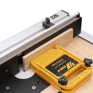 May include: A woodworking tool setup featuring a yellow feather-loc guide. The guide is on a wooden surface, with a light-coloured wood piece in place. The setup includes a silver rail and black components.